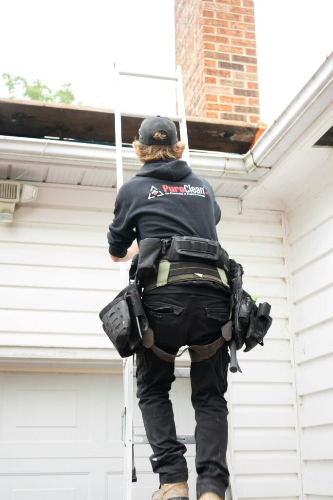 Roofer in safety gear climbs ladder for chimney inspection. Outdoor maintenance work.